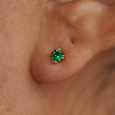 Close up view of a model's ear wearing a 14k yellow gold Emerald Earring
