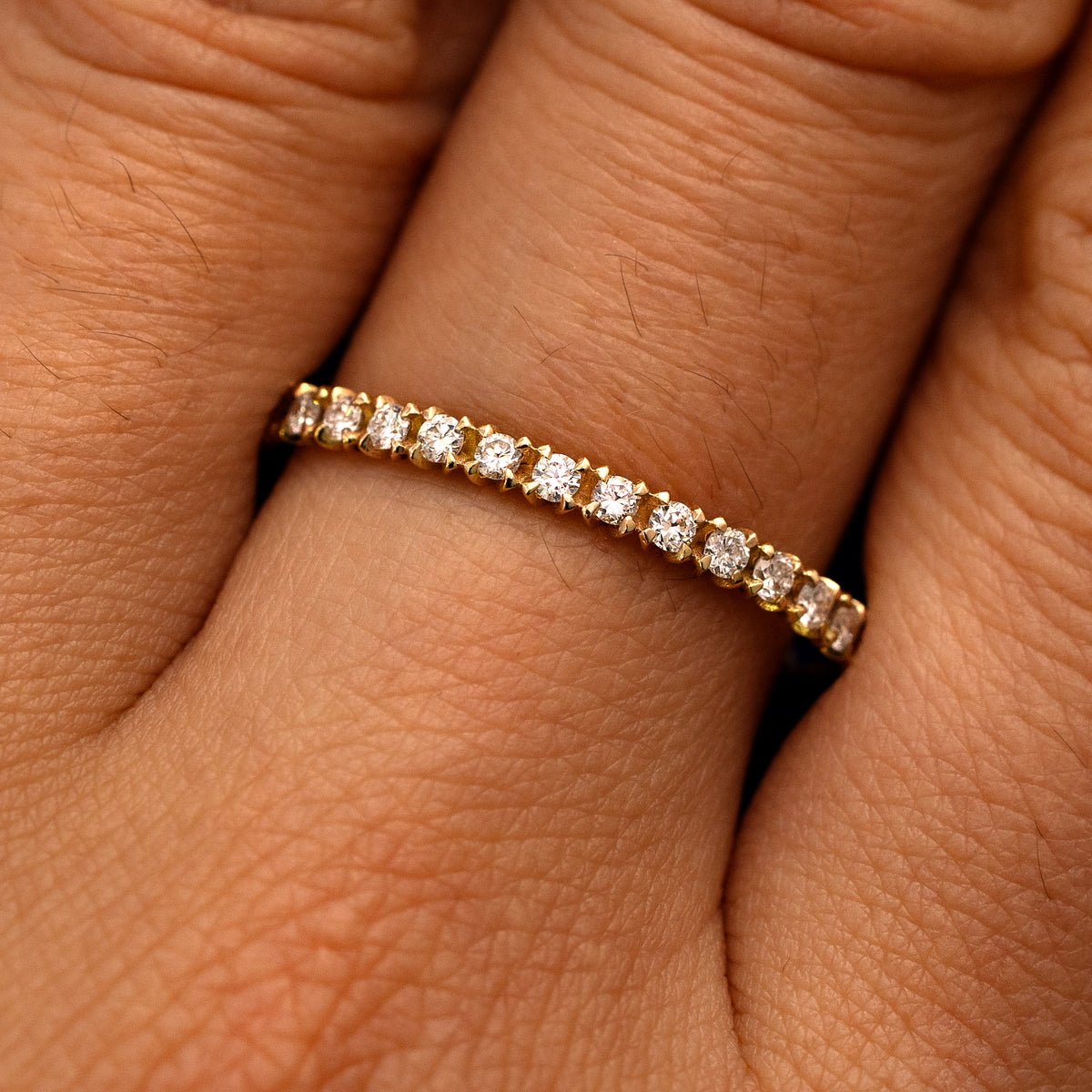 Close up view of a model's fingers wearing a 14k yellow gold Mini Petal Set Diamond Eternity Band
