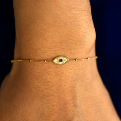 A close up view of a model's wrist wearing a yellow gold Evil Eye Bracelet on their hand