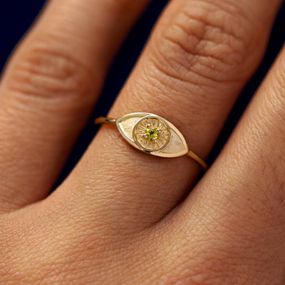 Close up view of a model's hand wearing a yellow gold Evil Eye Ring in the Emerald gemstone option