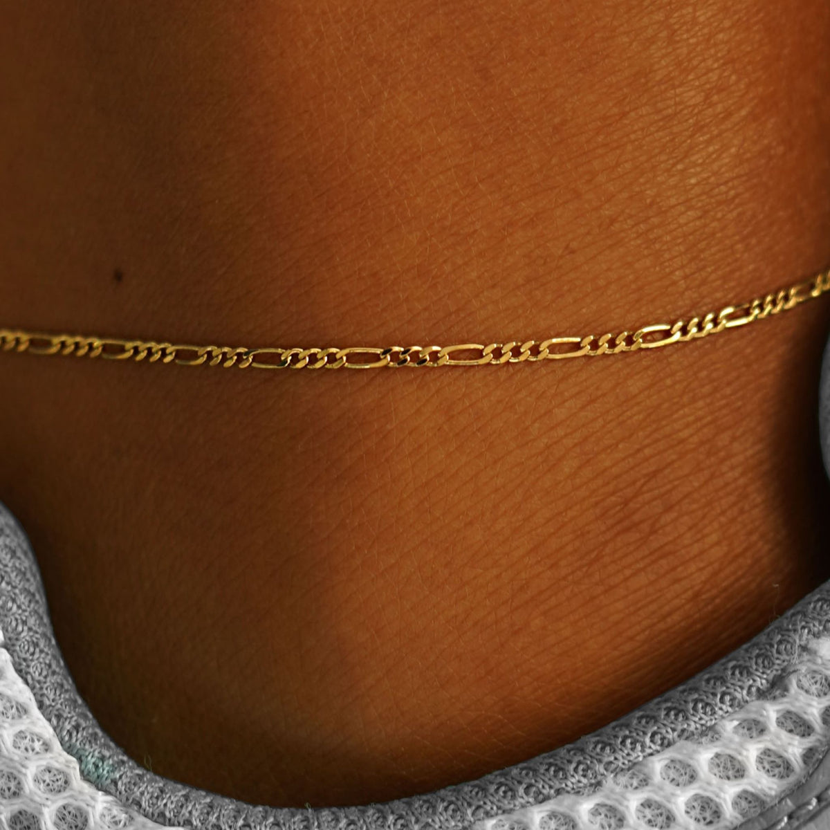 Close up view of a model's ankle wearing a yellow gold Figaro Anklet