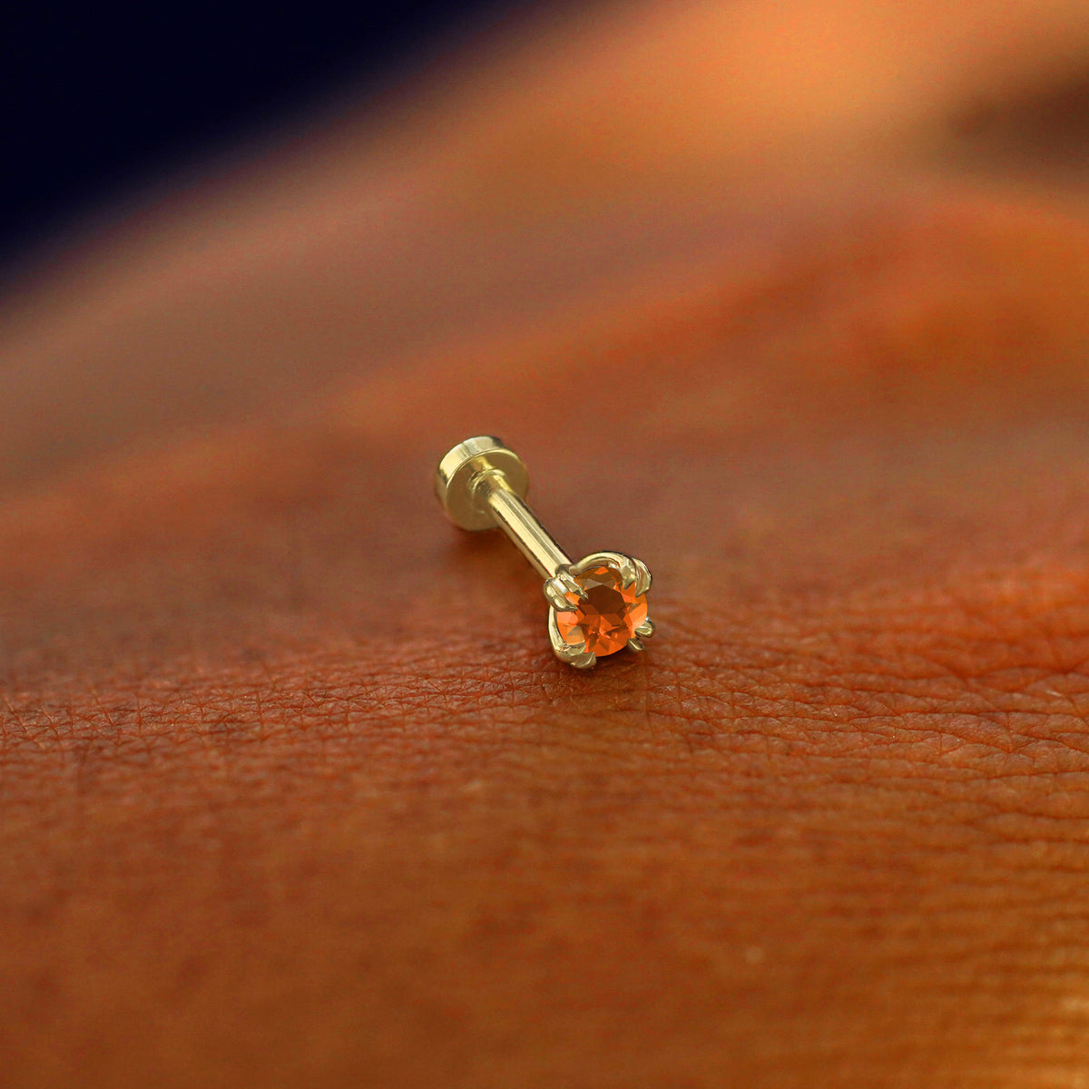 A solid 14k yellow gold Fire Opal Flatback Piercing resting on the back of a model's hand