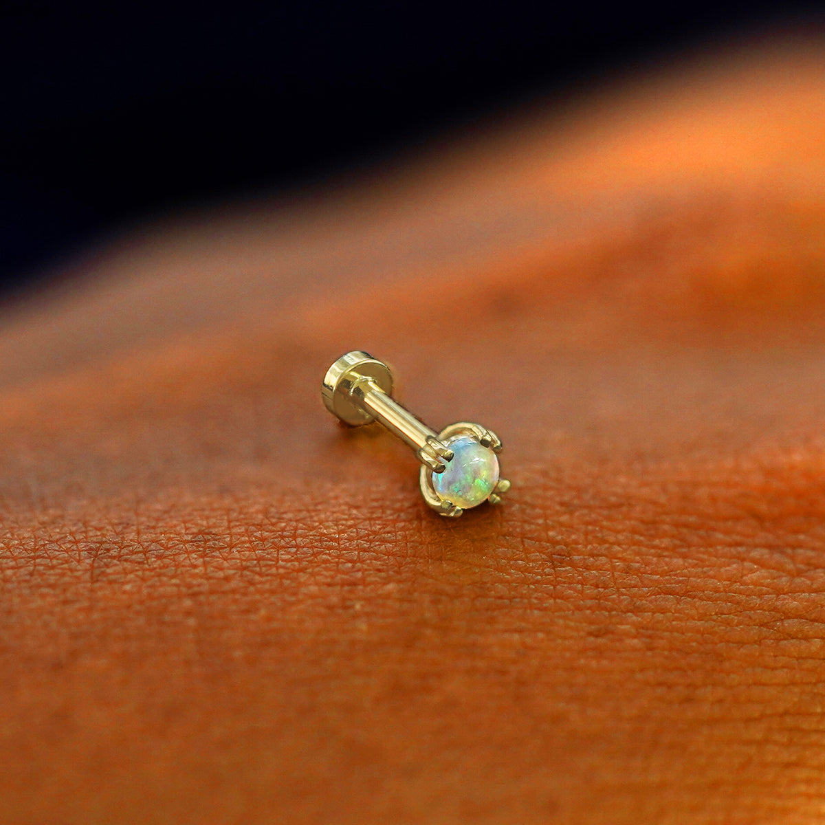 A solid 14k yellow gold Opal Flatback Piercing resting on the back of a model's hand