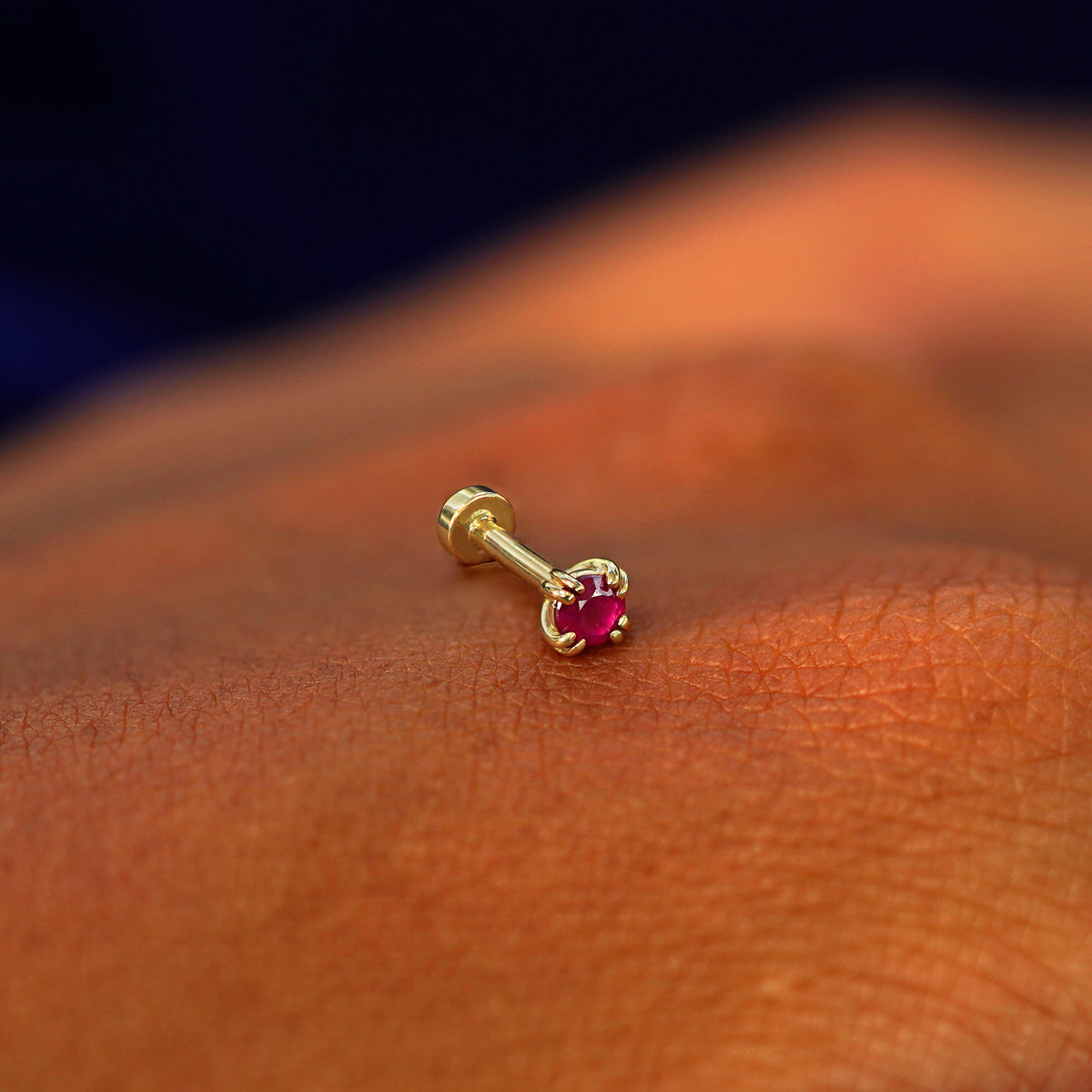 A solid 14k yellow gold Ruby Flatback Piercing resting on the back of a model's hand