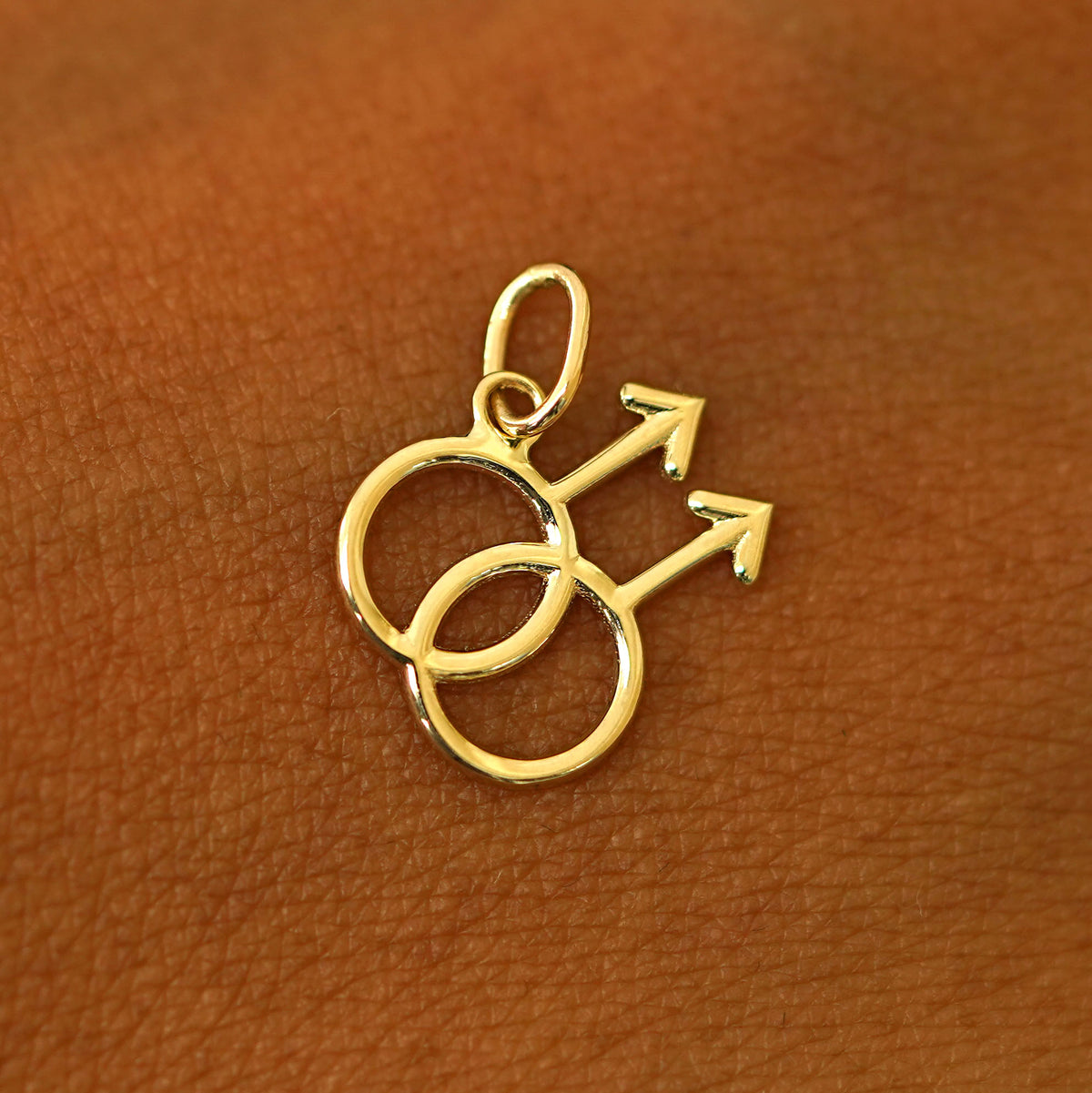 A solid 14k yellow gold Gay Symbol Charm resting on the back of a model's hand