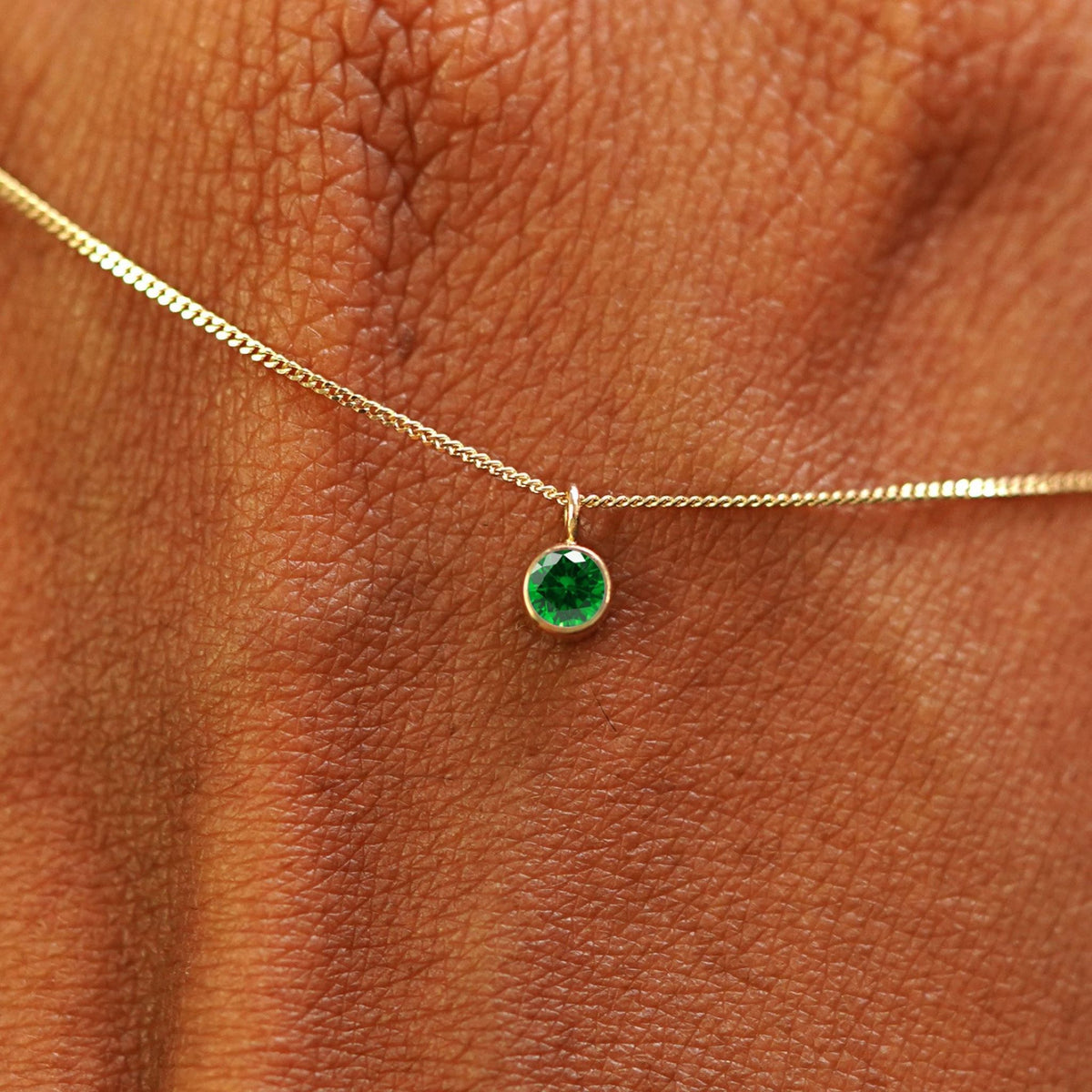 Close up view of a 14k yellow gold Emerald Necklace draped across the back of a model's hand