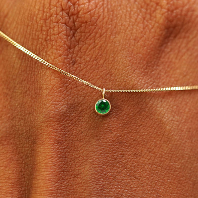 Close up view of a 14k yellow gold Emerald Necklace draped across the back of a model's hand