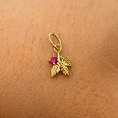 A solid 14k yellow gold ruby Gemstone 3 Leaves Charm resting on the back of a model's hand