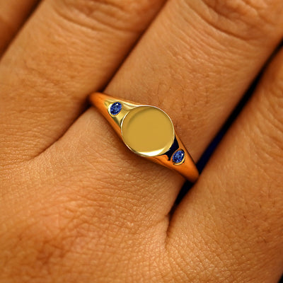 Close up view of a model's fingers wearing a 14k yellow gold Gemstone Signet Ring in sapphire