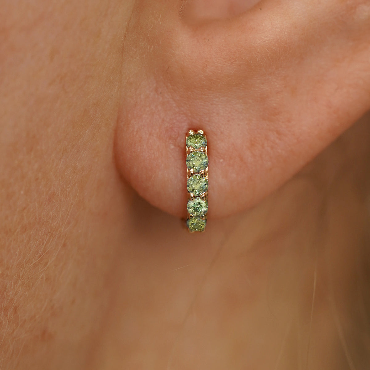 Close up view of a model's ear wearing a yellow gold Mini Light Green Lab Diamond Huggie Hoop