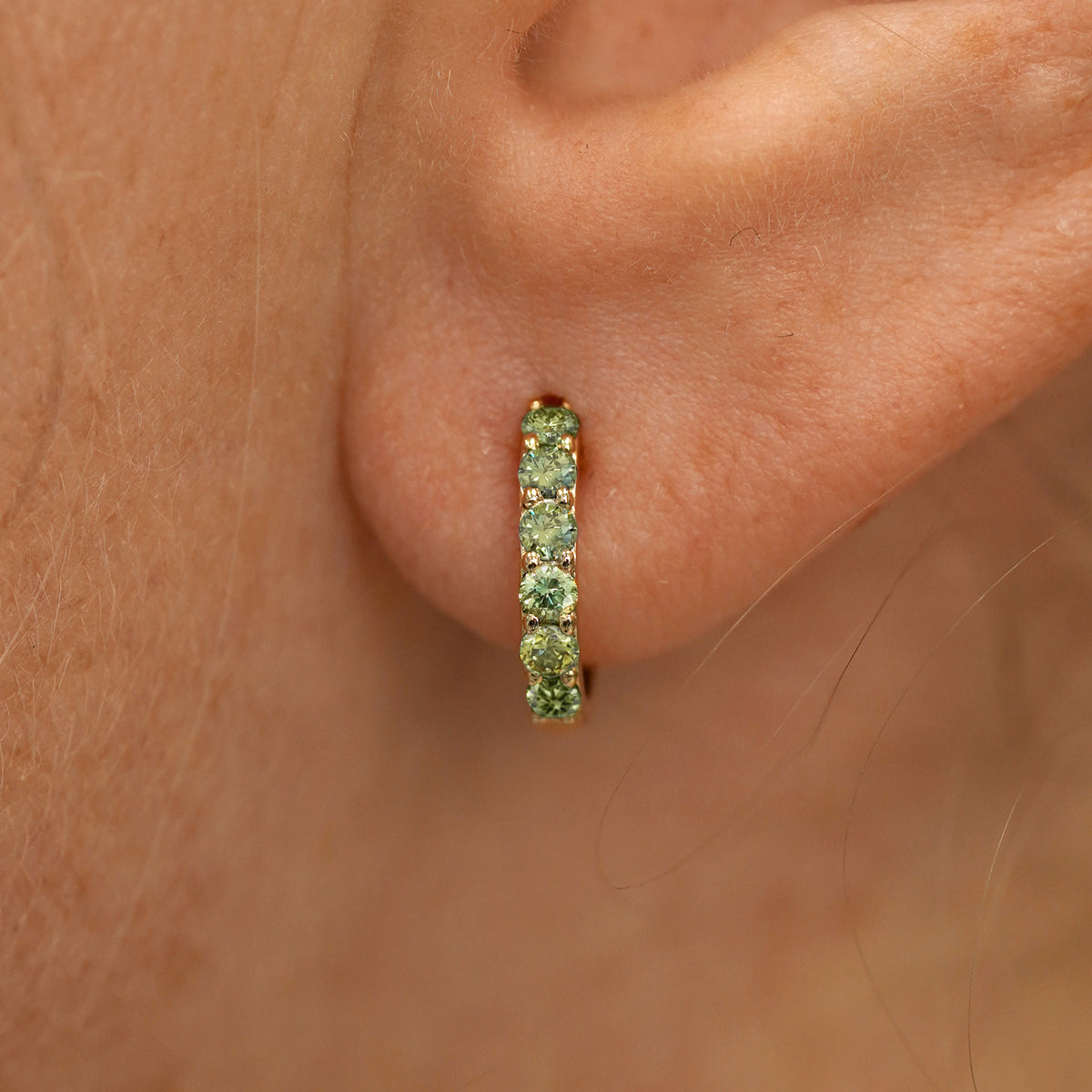 Close up view of a model's ear wearing a yellow gold Small Light Green Lab Diamond Huggie Hoop