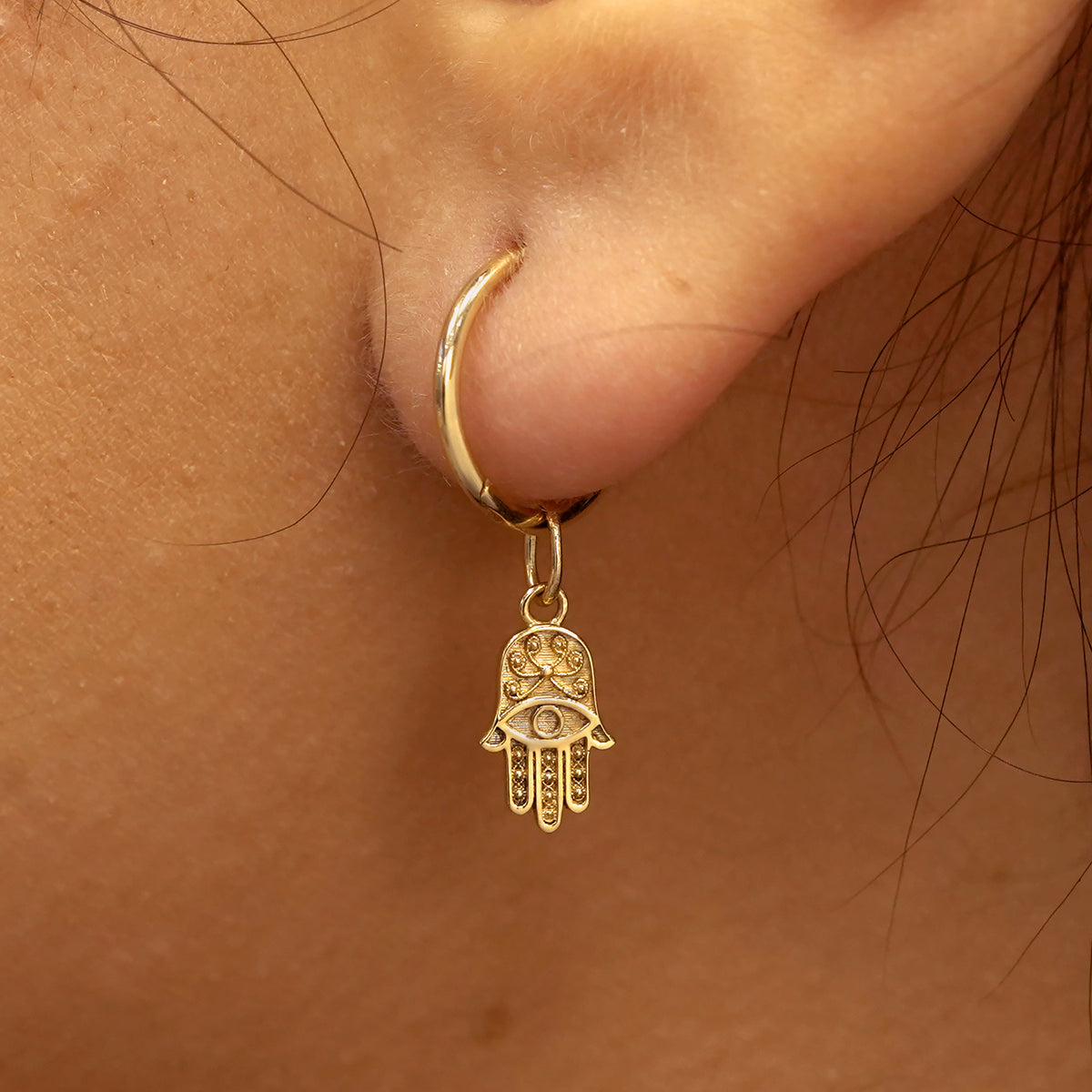 Close up view of a model's ear wearing a yellow gold Hamsa hand charm on a Small Seamless Huggie Hoop
