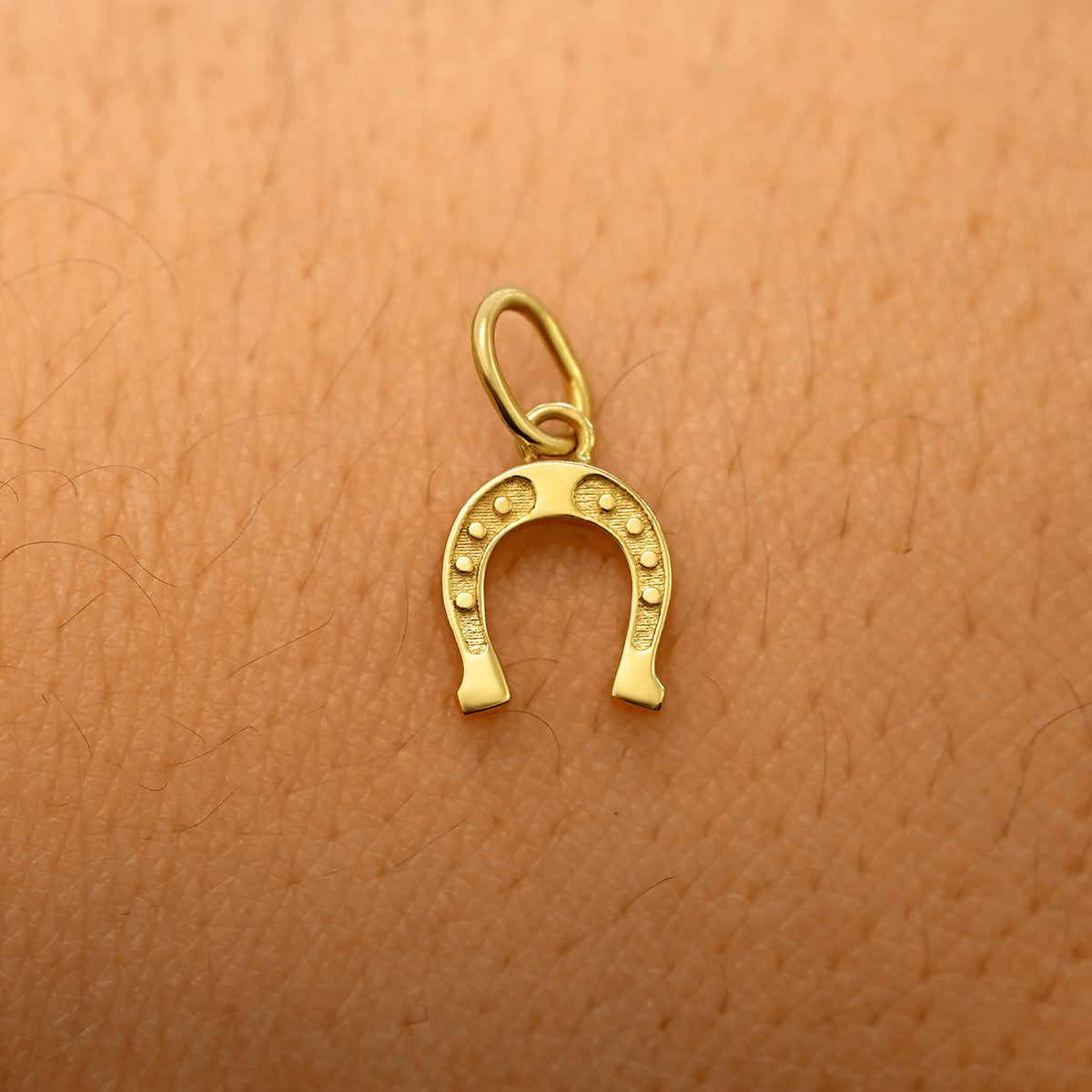 A solid 14k yellow gold Horseshoe Charm resting on the back of a model's hand