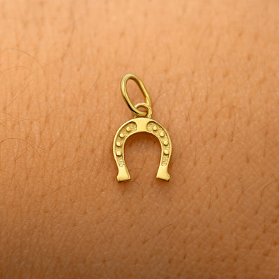 A solid 14k yellow gold Horseshoe Charm resting on the back of a model's hand