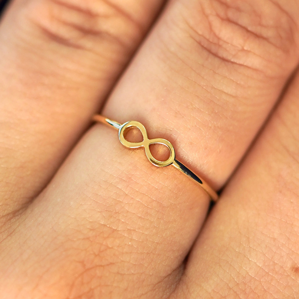 Close up view of a model's fingers wearing a 14k yellow gold Infinity Ring
