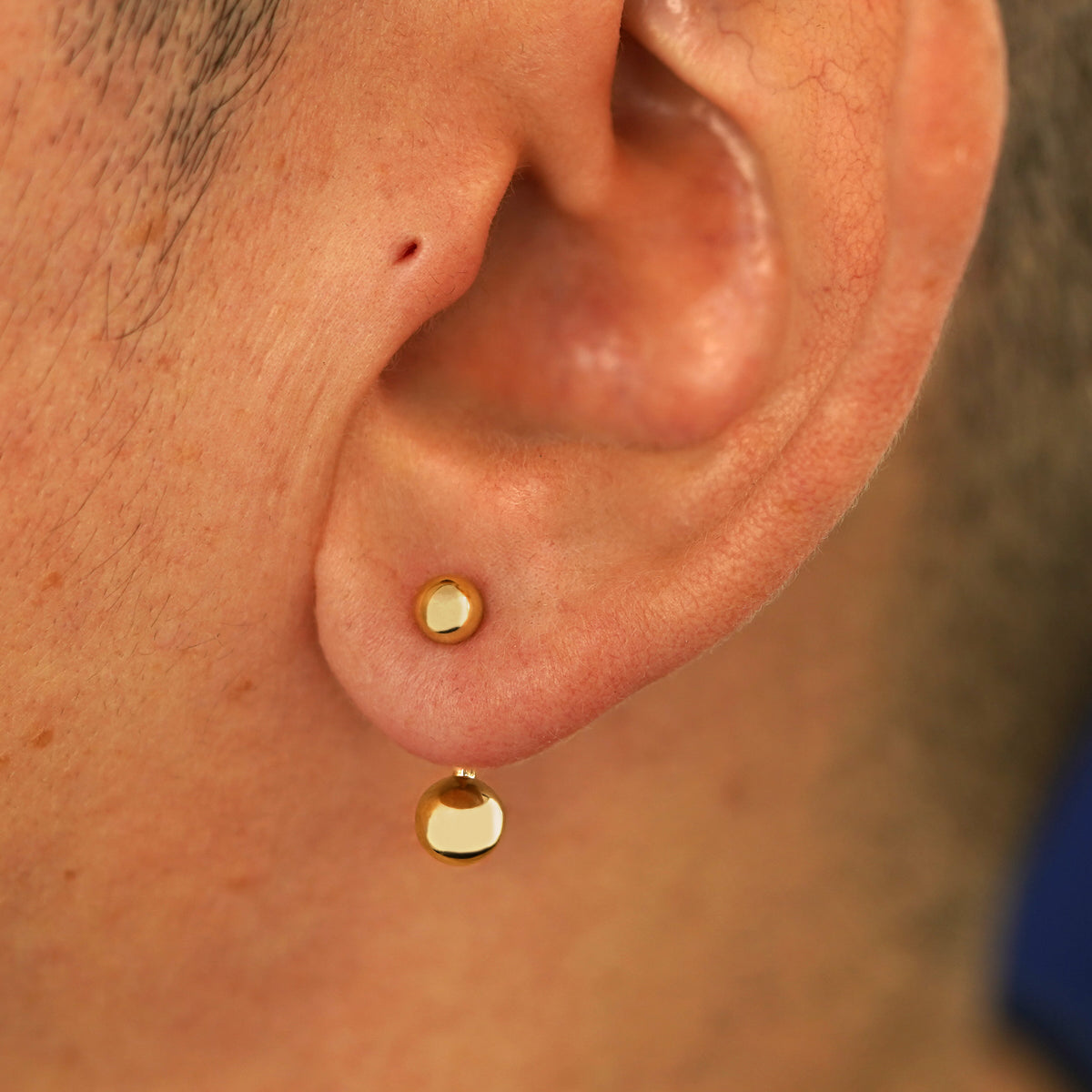 Close up view of a model's ear wearing a 14k yellow gold Large Curved Barbell through a lobe piercing