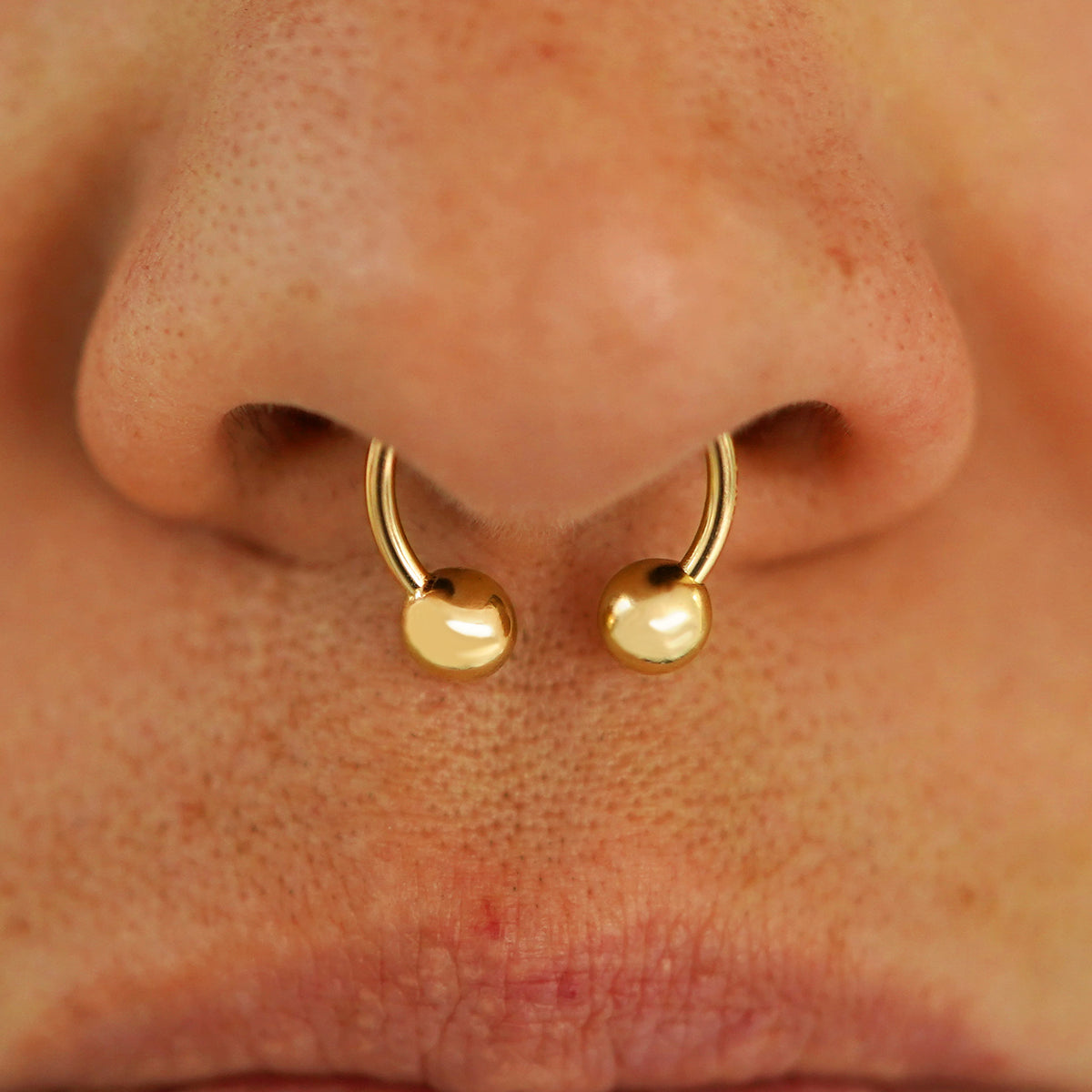 Close up view of a model's nose wearing a 14k yellow gold Medium Horseshoe in a septum piercing