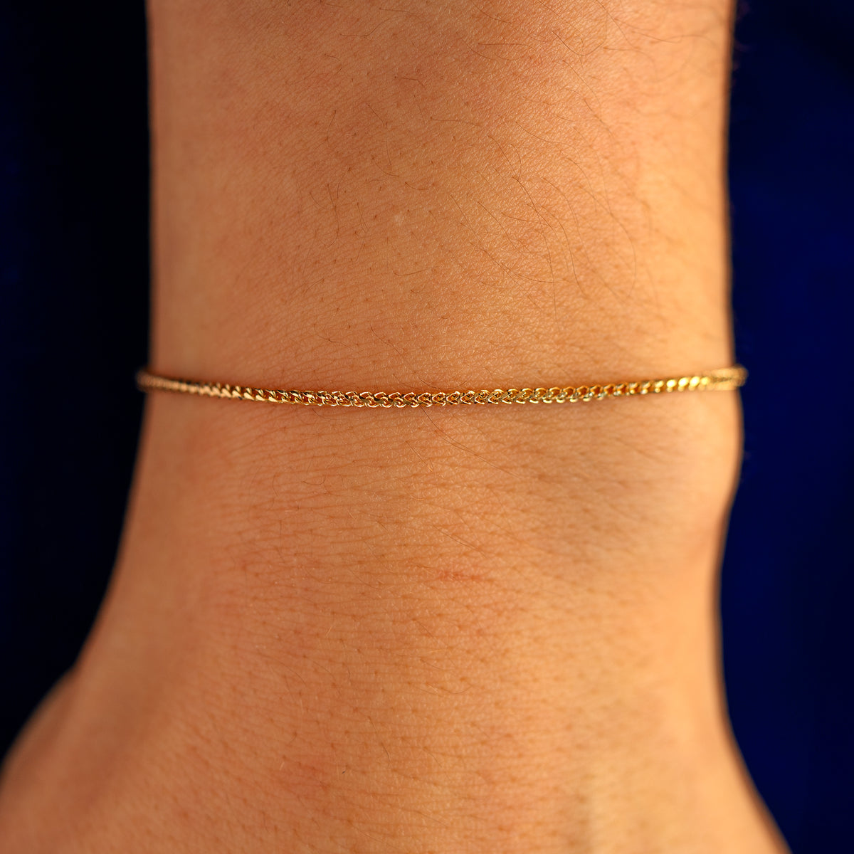 Close up view of a models wrist wearing a solid 14k yellow gold Mini Franco Chain Bracelet