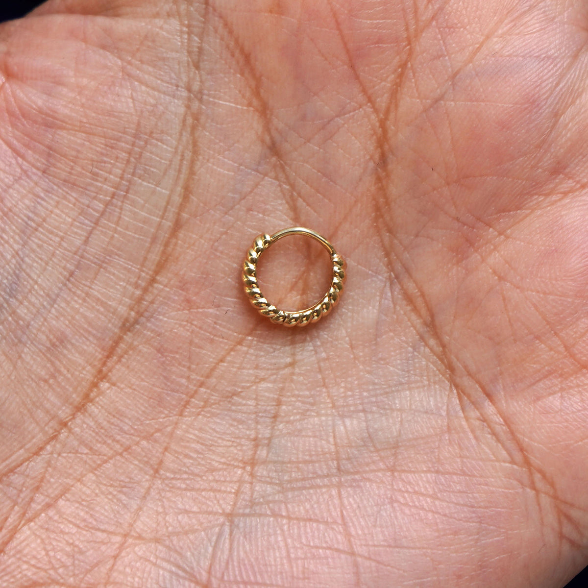 A solid 14k yellow gold Mini Rope Huggie Hoop Earring closed in a model's palm