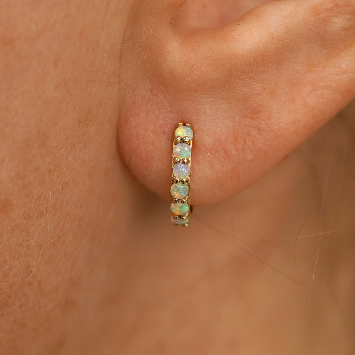Close up view of a model's ear wearing a yellow gold Small Opal Huggie Hoop