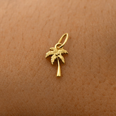 A solid 14k yellow gold Palm Tree Charm resting on the back of a model's hand