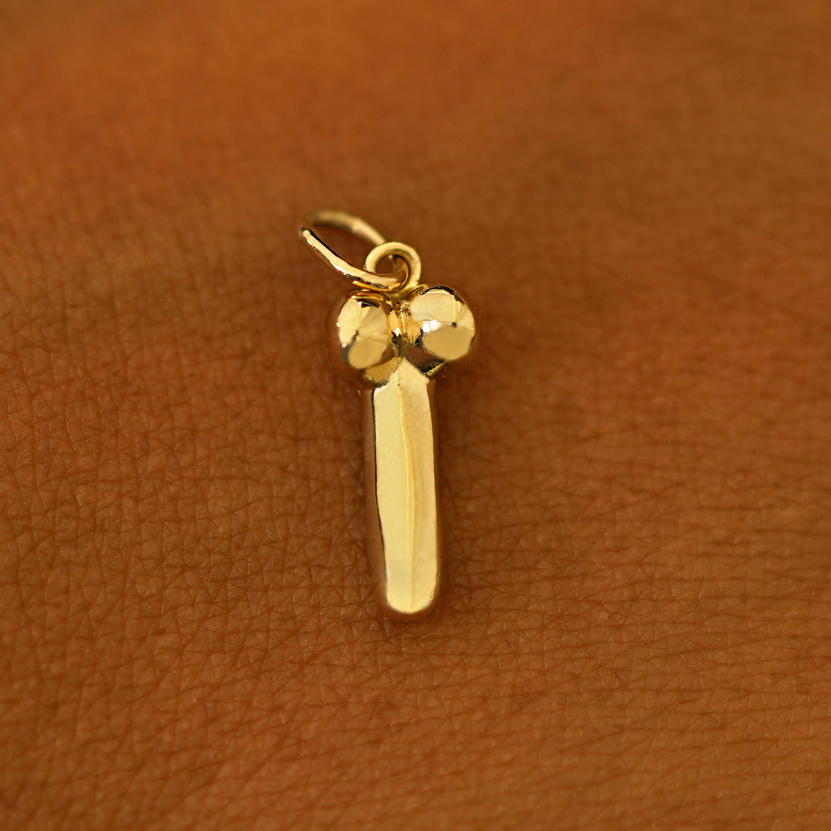 A 14k yellow gold penis charm on the back of a models hand
