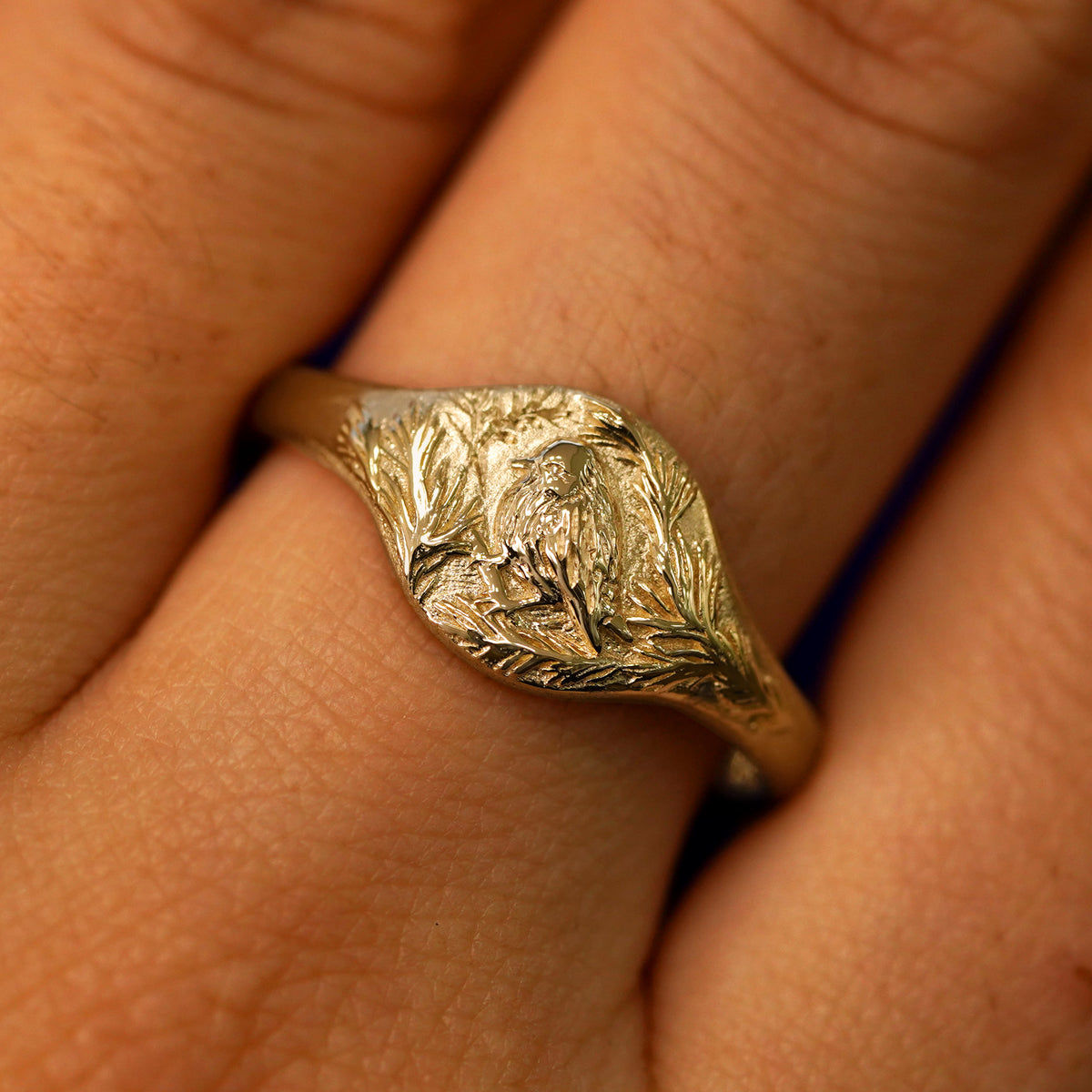 Close up view of a model's fingers wearing a 14k yellow gold Pine and Bird Signet Ring