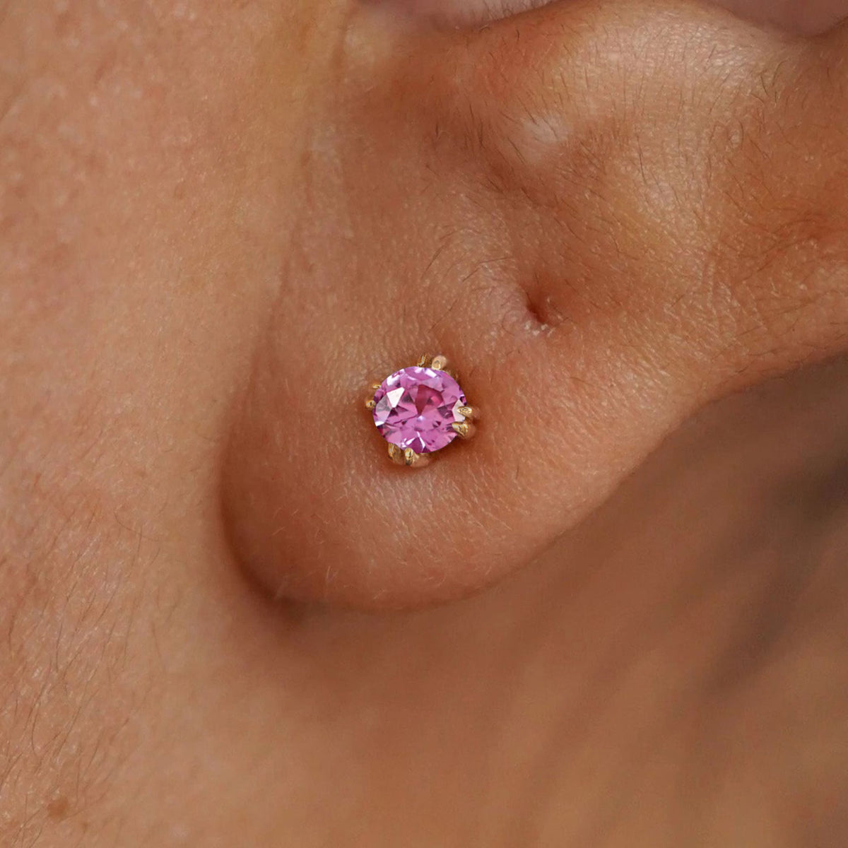 Close up view of a model's ear wearing a 14k yellow gold Pink Sapphire Earring