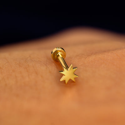 A yellow gold 8 pointed star flatback piercing with yellow gold backing on a models hand