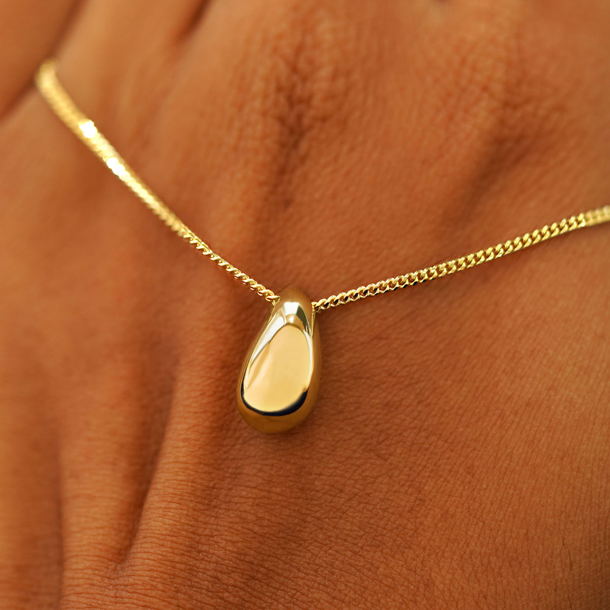 A model's holding a yellow gold Puffy Teardrop Necklace across the back of their hand