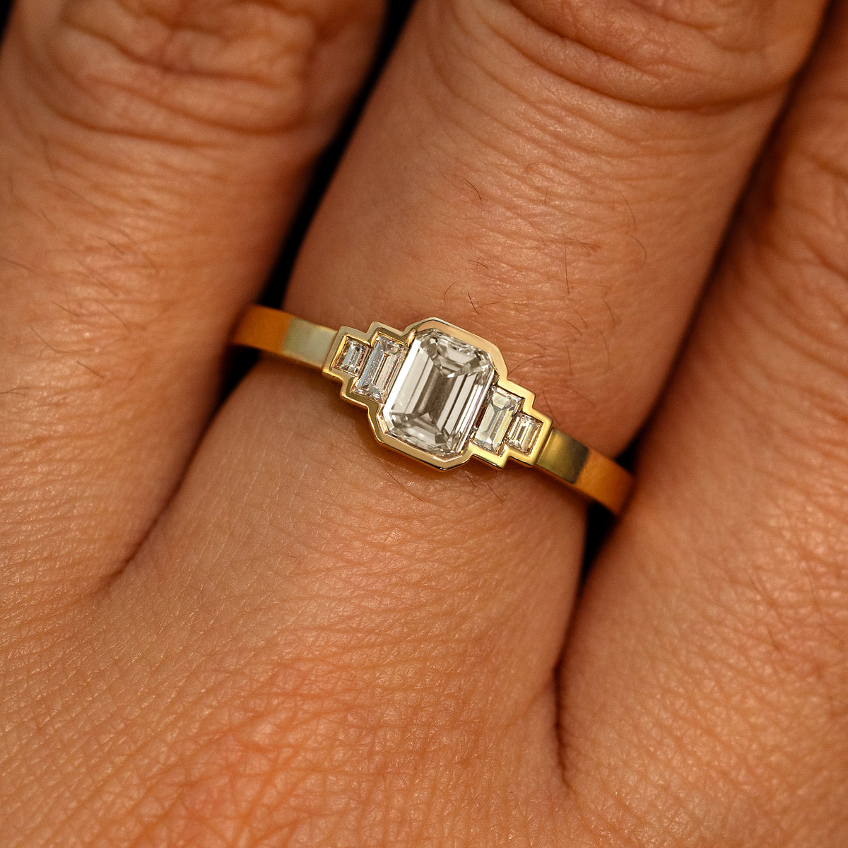 Close up view of a model's hand wearing a 14k yellow gold Emerald Cut and Baguette Diamond Ring