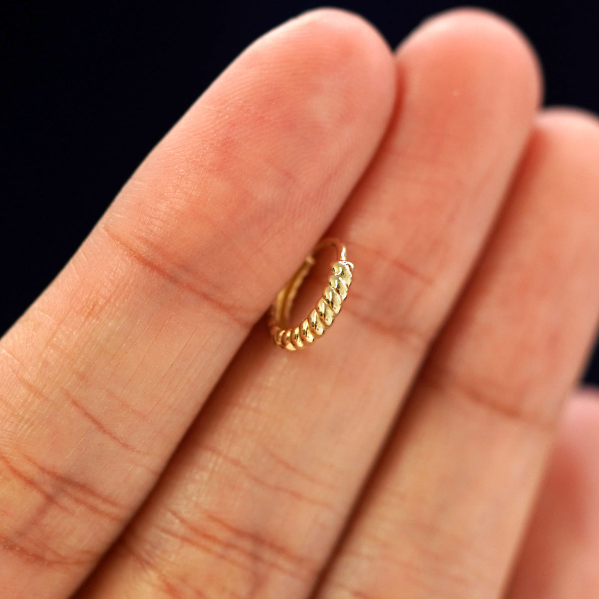 A 14k gold Mini Rope Huggie Hoop Earring held in between a model's fingers to show the hoops thickness