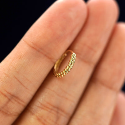 A 14k gold Small Rope Huggie Hoop Earring held in between a model's fingers to show the hoops thickness
