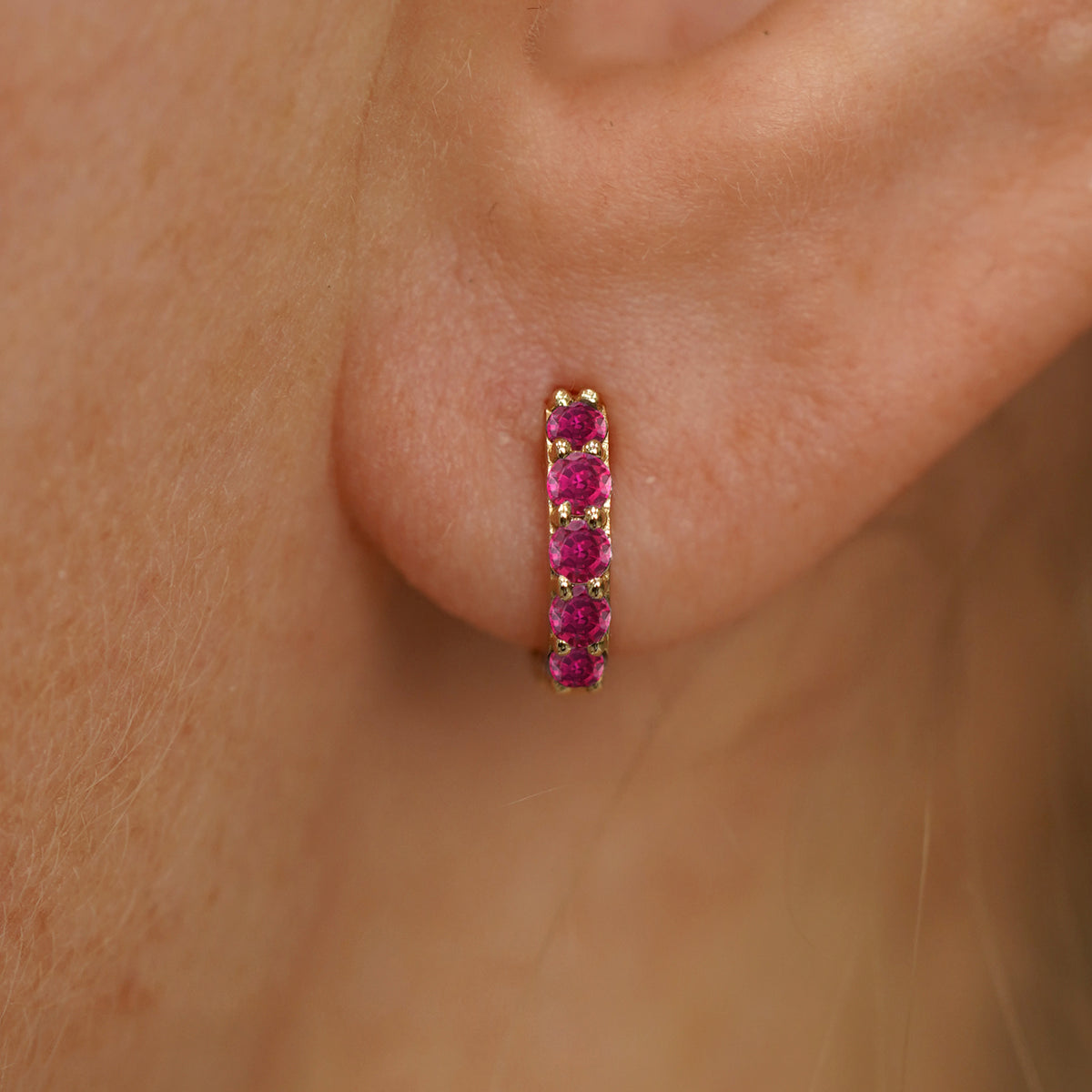Close up view of a model's ear wearing a yellow gold Mini Ruby Huggie Hoop