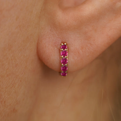 Close up view of a model's ear wearing a yellow gold Mini Ruby Huggie Hoop