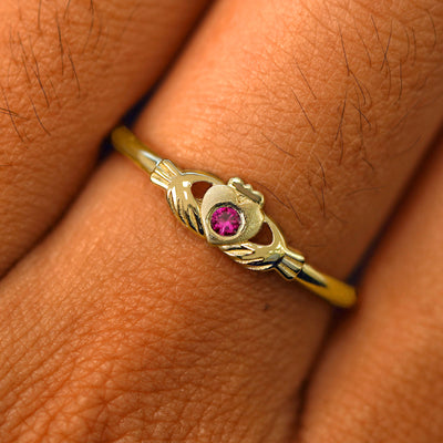 Close up view of a model's fingers wearing a 14k yellow gold ruby Thin Gemstone Claddagh Ring