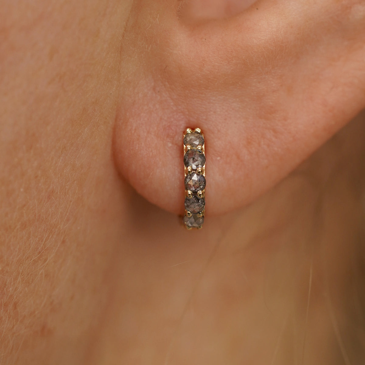 Close up view of a model's ear wearing a yellow gold Mini Salt and Pepper Diamond Huggie Hoop