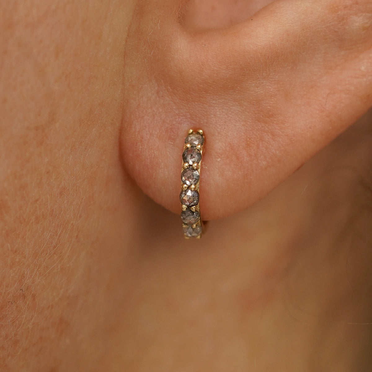 Close up view of a model's ear wearing a yellow gold Small Salt and Pepper Diamond Huggie Hoop