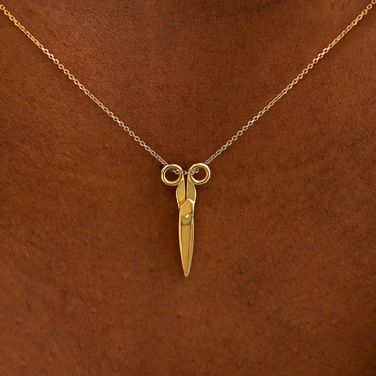 Close up view of a model's neck wearing a solid 14k yellow gold Scissors Necklace