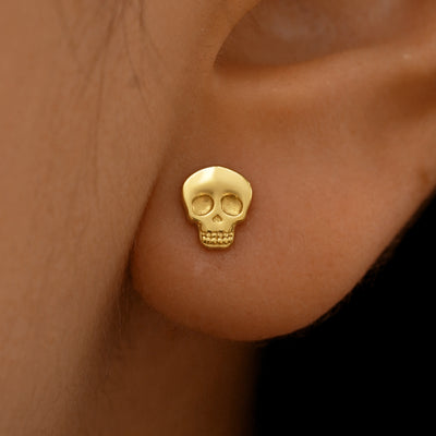 Close up view of a model's ear wearing a 14k yellow gold Skull Earring