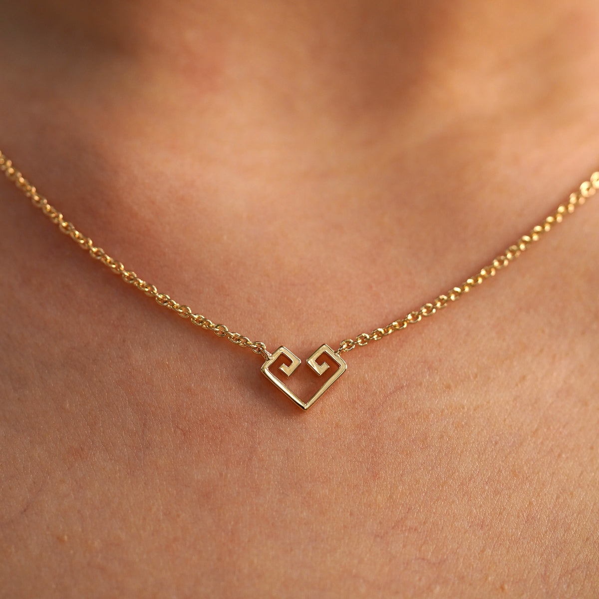A close up view of a model's neck wearing a yellow gold Small Chere Heart Necklace