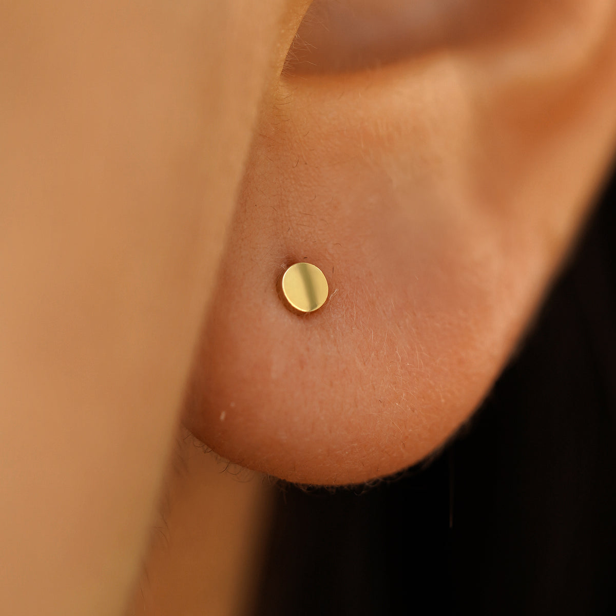 Close up view of a model's ear wearing a small circle Earring in Yellow Gold.