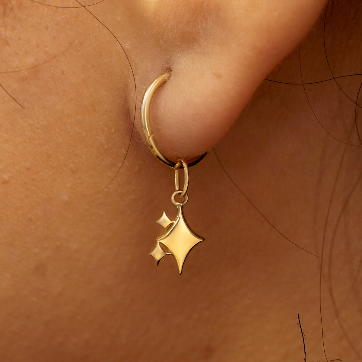 Close up view of a model's ear wearing a yellow gold Sparkly Emoji Charm on a Small Seamless Huggie Hoop