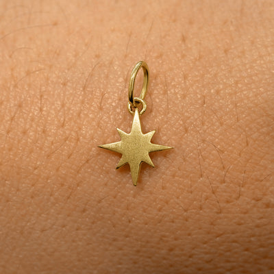 A solid 14k yellow gold Starburst Charm resting on the back of a model's hand