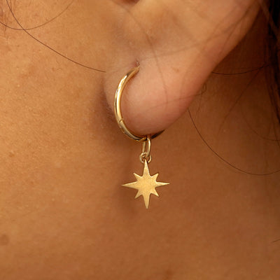 Close up view of a model's ear wearing a yellow gold Starburst Charm on a Small Seamless Huggie Hoop