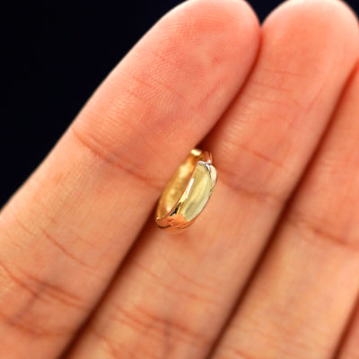 A 14k gold Small Thick Huggie Hoop Earring held in between a model's fingers to show the hoops thickness