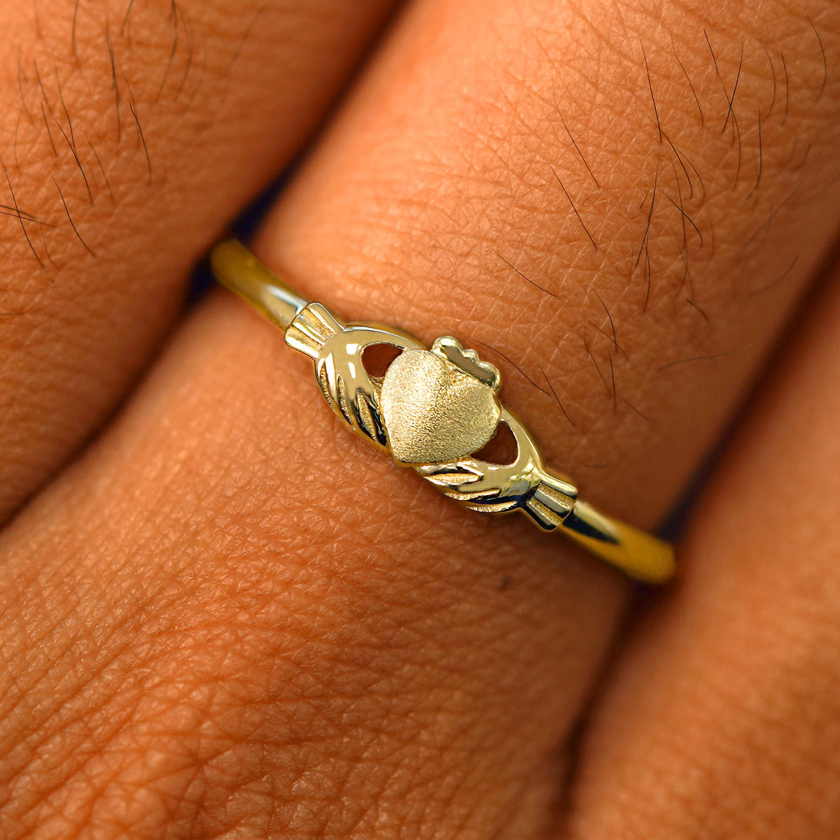 Close up view of a model's fingers wearing a 14k yellow gold Thin Claddagh Ring