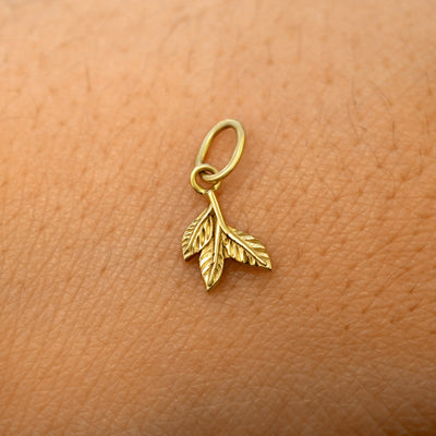 A solid 14k yellow gold 3 Leaves Charm resting on the back of a model's hand