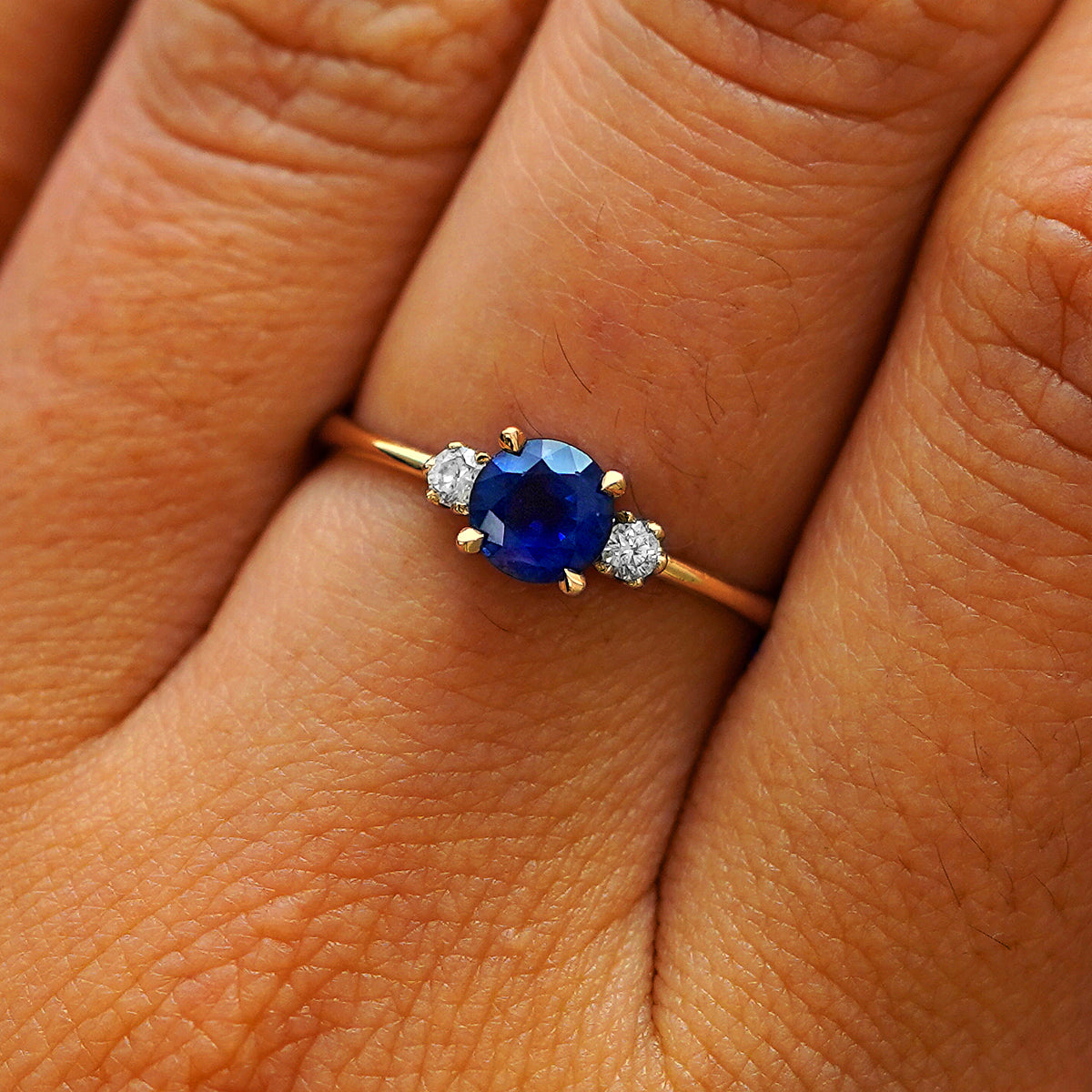 Close up view of a model's hand wearing a 14k yellow gold three stone sapphire ring