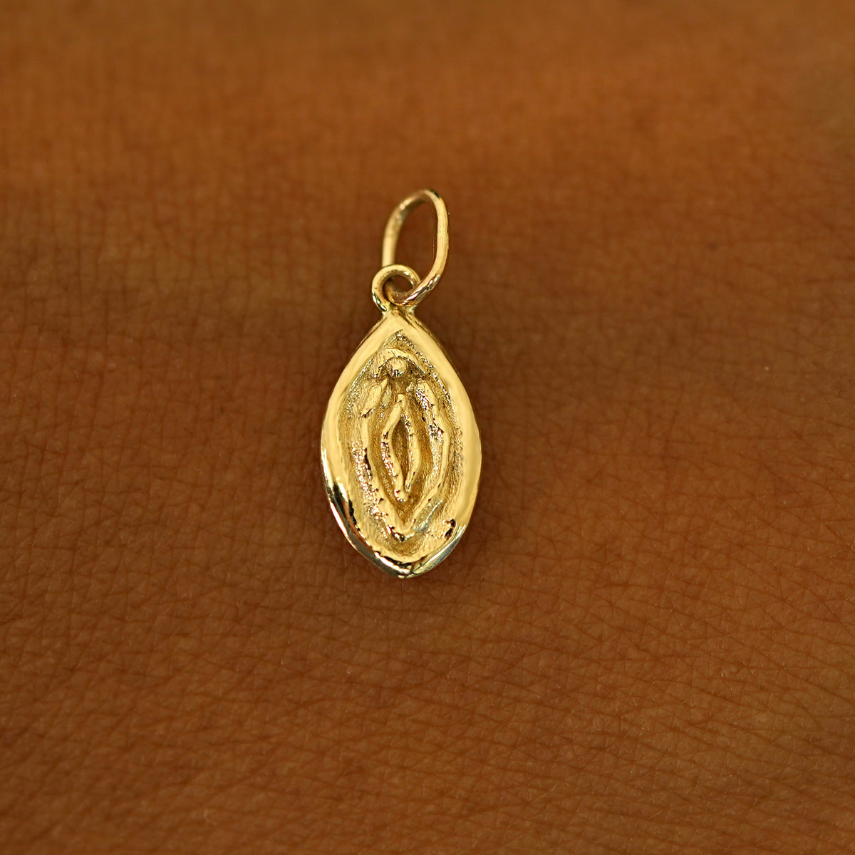 A solid 14k yellow gold Vulva Charm resting on the back of a model's hand